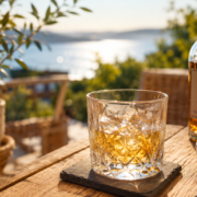 Verre de whisky servi en terrasse en été avec vue lumineuse sur l’eau pour illustrer la dégustation du whisky par temps chaud